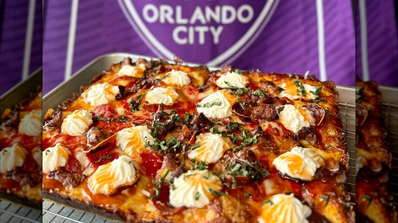 Detroit-style pizza on a metal baking tray with a purple Orlando City flag