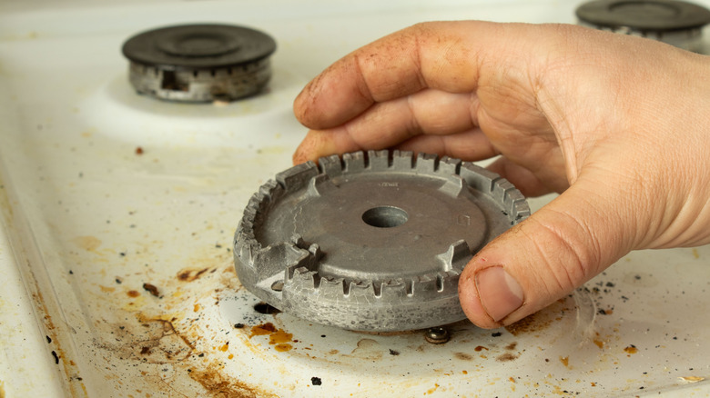 A person removing a dirty burner head from a gas stove to clean it
