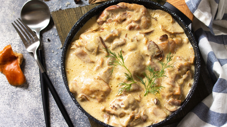 A skillet of creamy chicken fricassee with utensils on the side