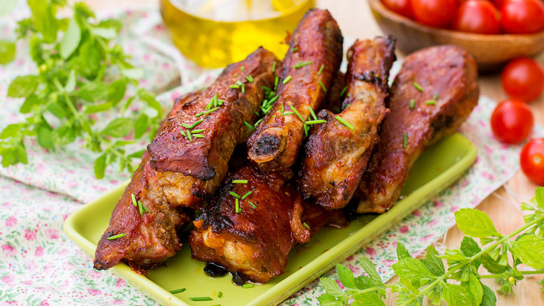 Country-style pork ribs on a green tray on top of a table with herbs and tomatoes