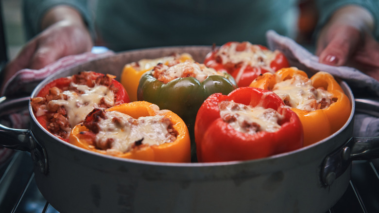 hands removing a pot of stuffed bell peppers from the oven