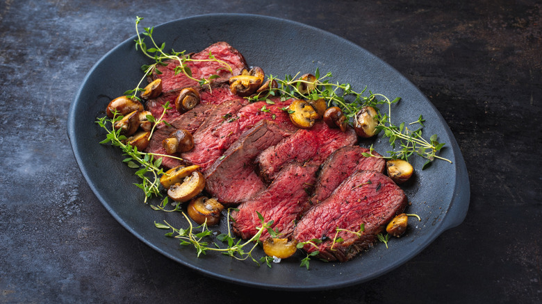 A plate with thin steak slices, accompanied by mushrooms and a herbal garnish.