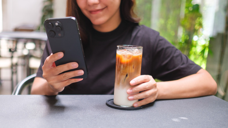 Young adult using a smartphone while holding an iced coffee