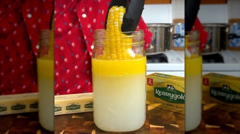 Person using tongs to dip a cob of corn into melted butter on top of water in a mason jar