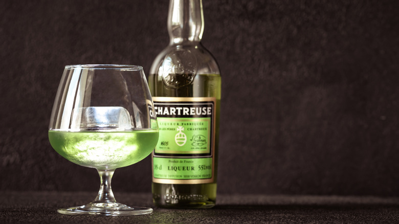 Chartreuse on the rocks in snifter next to Chartreuse bottle against black background
