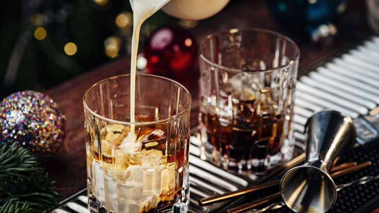 Smooth and creamy white Russian is being made on bar rail with two rocks glasses of dark brown spirit with cream poured overtop
