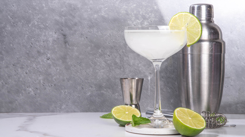 Gimlet citrus alcohol cocktail with gin or vodka and lime garnish, on light grey with hard light and bar utensils