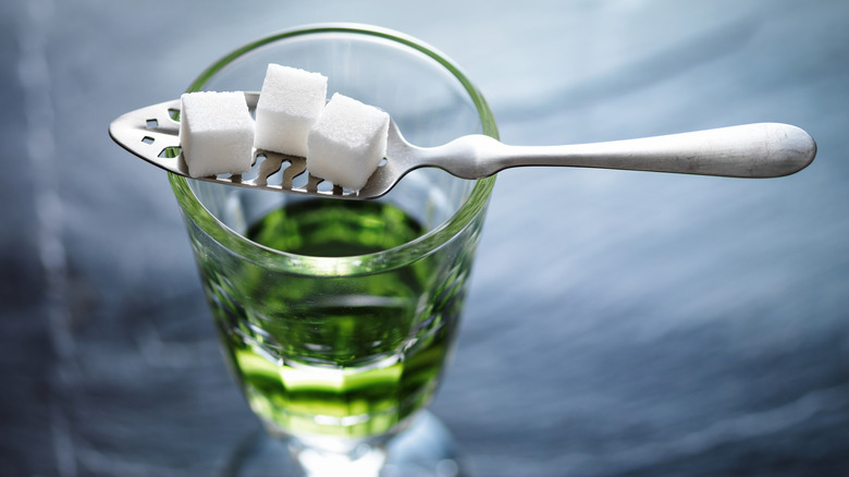 An absinthe spoon holding sugar cubes sitting atop a glass with absinthe in it