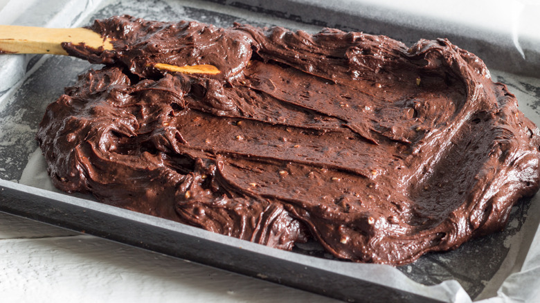 brownie batter being spread into a pan with a wooden spoon