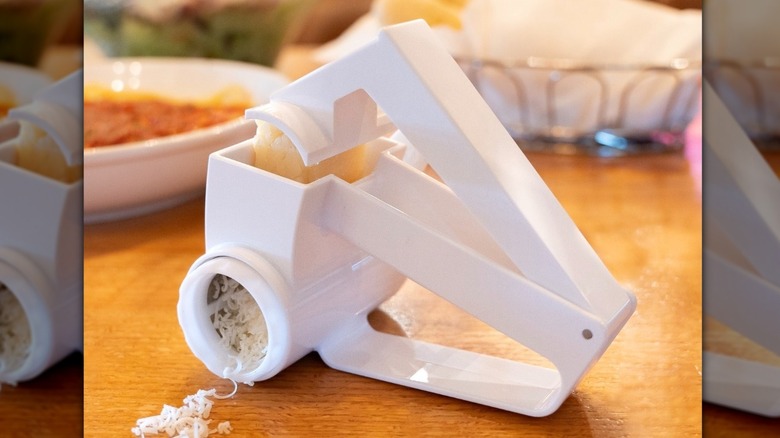 A sprinkle of grated cheese set in front of an Olive Garden grater on a table of food