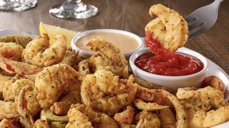 A fork dunks a piece of Shrimp Fritto Misto into sauce as steam rises over the plate