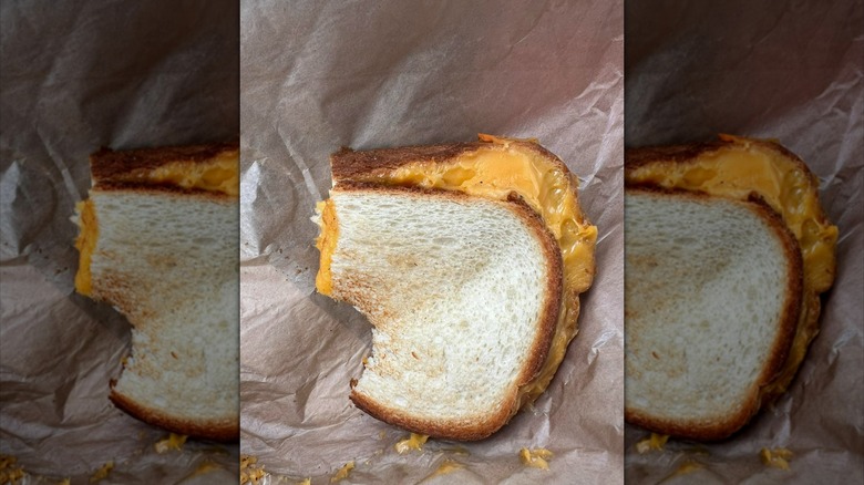 Bitten, partially-melted grilled cheese sandwich on parchment paper