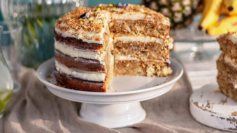 Hummingbird cake on cake platter with pineapple and bananas in the background