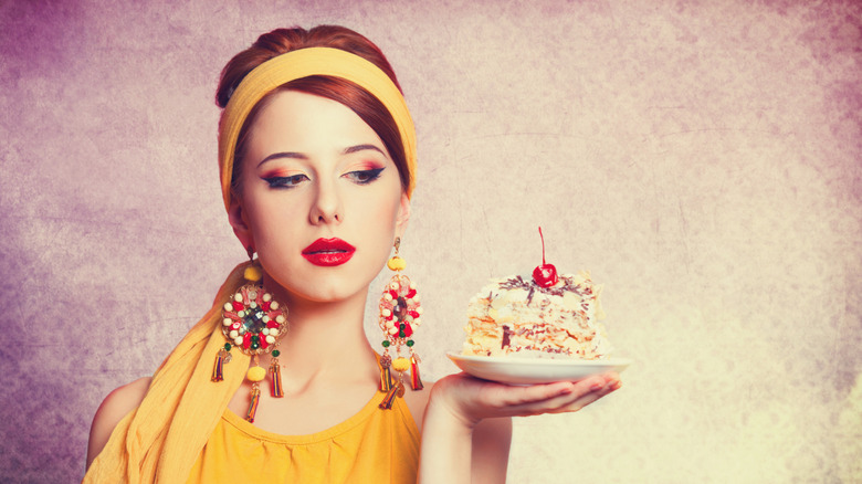 Stylish retro woman with cake on saucer in hand