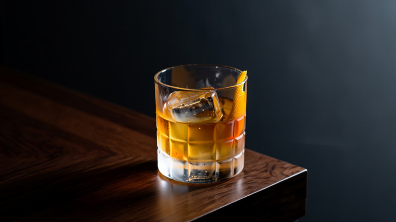 A single old fashioned cocktail on the corner of a wooden table