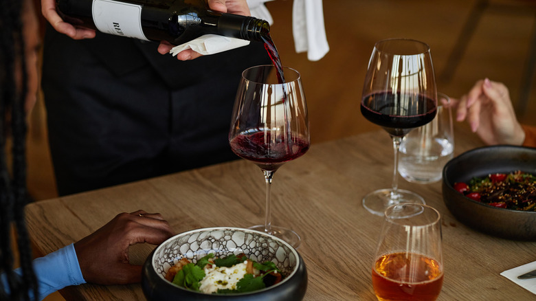 A waiter pouring red wine into wine glasses at a dining table