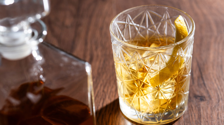 Rusty Nail cocktail with lemon peel in a crystal glass on a wooden table