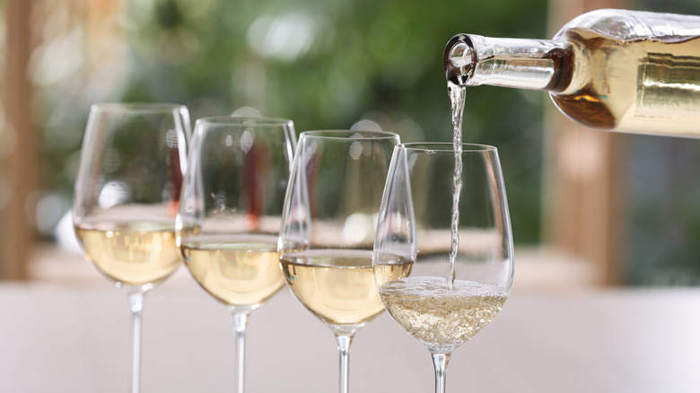 A bottle of white wine being poured into four wine glasses