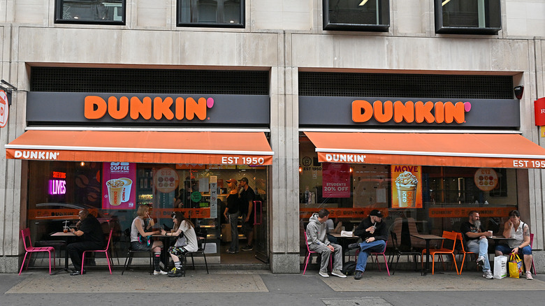 Diners eat at tables situated outside a physical Dunkin' storefront.