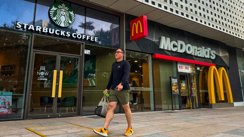 A pedestrian walks by two physical storefronts for Starbucks and McDonald's.