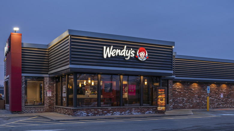 The exterior of a brick Wendy's location is pictured against a darker blue sky.