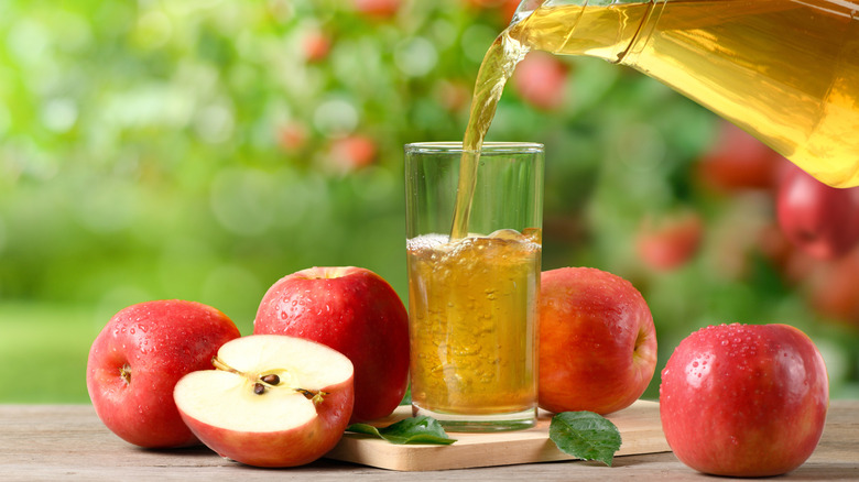Apple juice pouring from a pitcher into a glass surrounded by apples