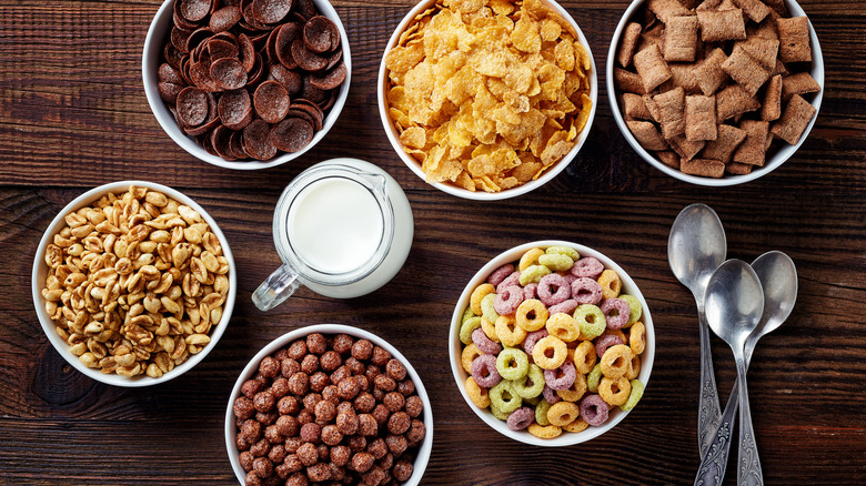 Various types of cereal in bowls with milk and spoons alongside