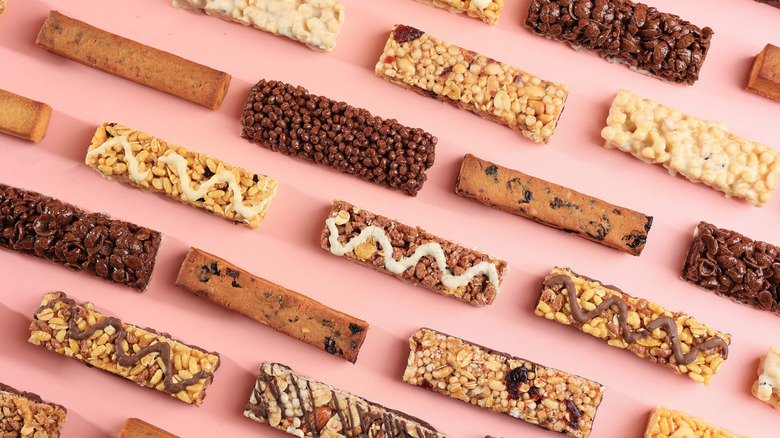 Different types of protein bars out of their wrappers on a pink background