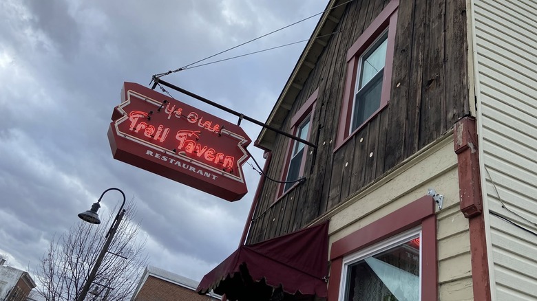 Neon sign for Ye Olde Trail Tavern jutting out from the wood and siding exterior on an overcast day