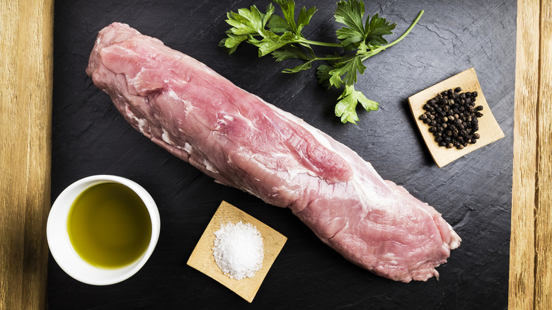 Raw pork tenderloin with other ingredients on black board