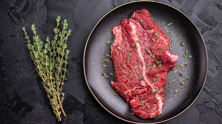Raw skirt steak on black plate next to bundle of rosemary