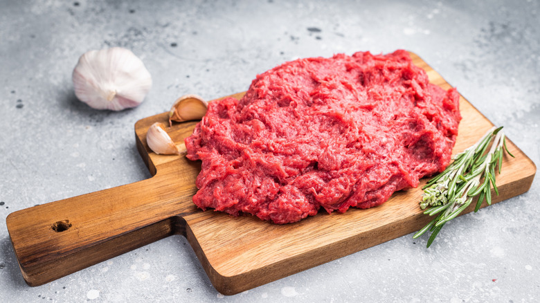 Raw ground venison on wooden board with sprig of rosemary