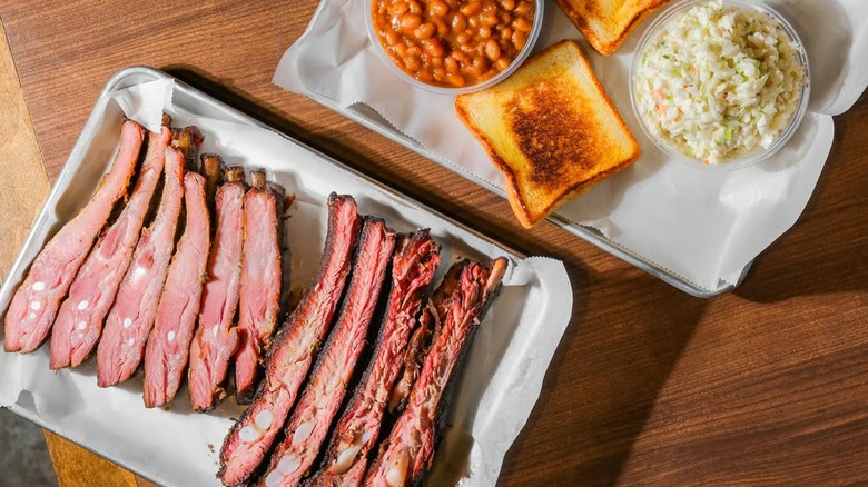 Tray of pork spare ribs and another tray of beans, toast, and coleslaw
