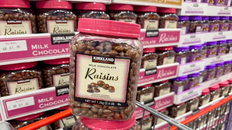 Close-up of a tub of Kirkland Signature Milk Chocolate Raisins in front of a shelf full of tubs.