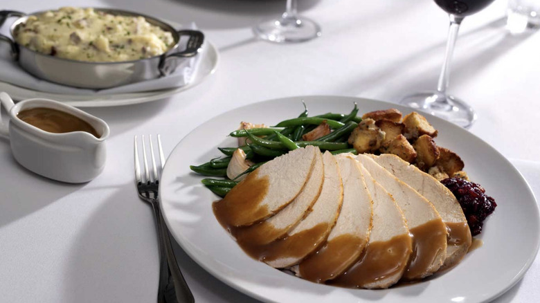 Turkey with gravy, green beans and stuffing on a plate above a white tablecloth