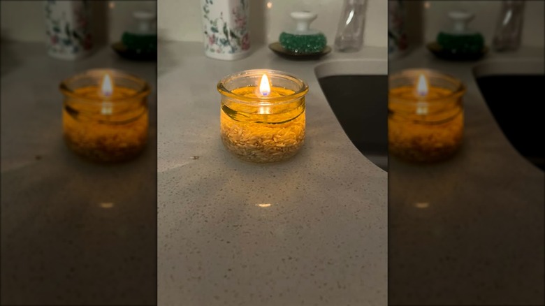 A homemade oil lamp constructed with white rice, olive oil, and a Q-tip burning on a kitchen counter