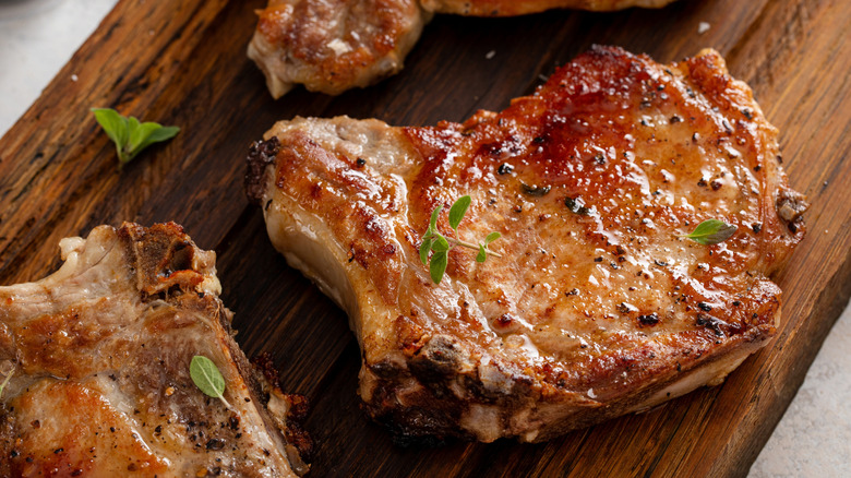 seared bone-in pork chops garnished with fresh herbs on a wooden board