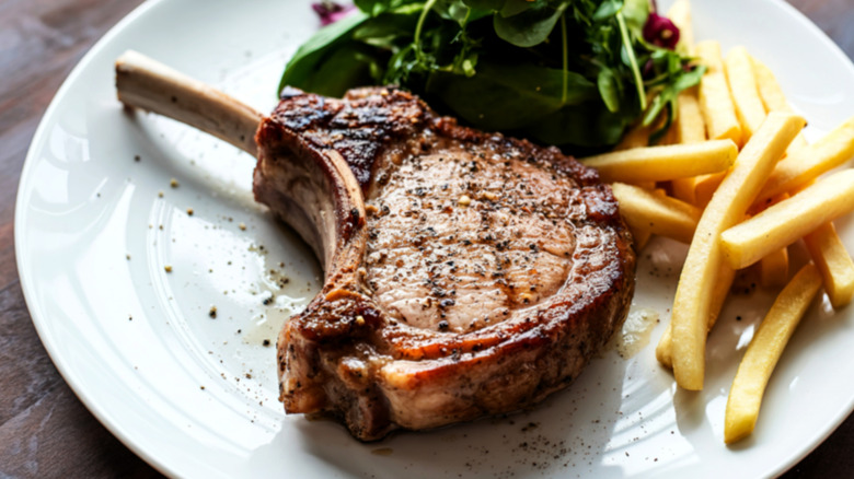 bone-in pork chop on a plate with french fries and greens