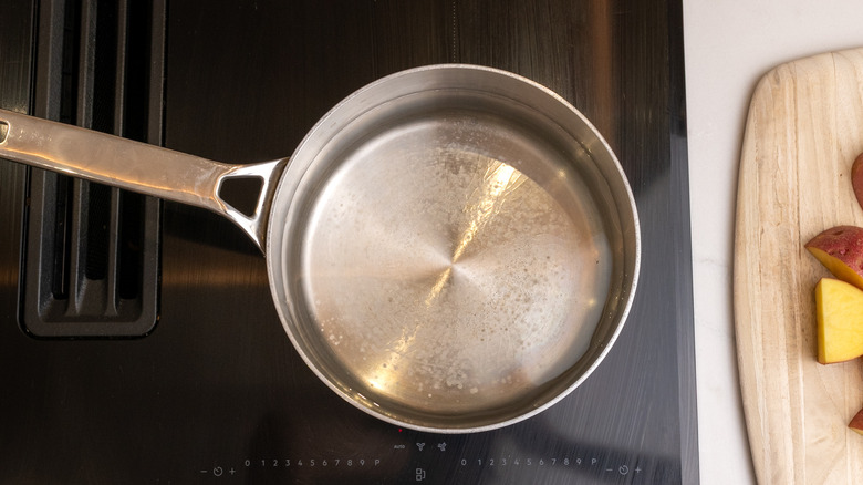saucepan of water cooking on hob next to chopped potatoes