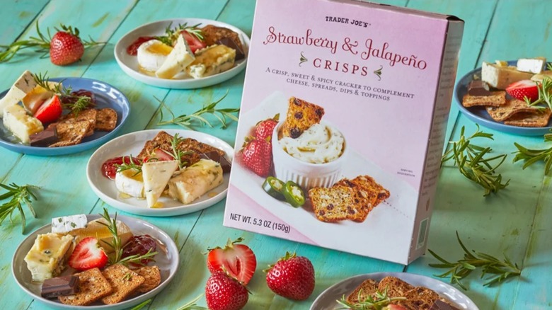 A box of strawberry & jalapeño crisps surrounded by small plates of cheese, fruit, and herbs