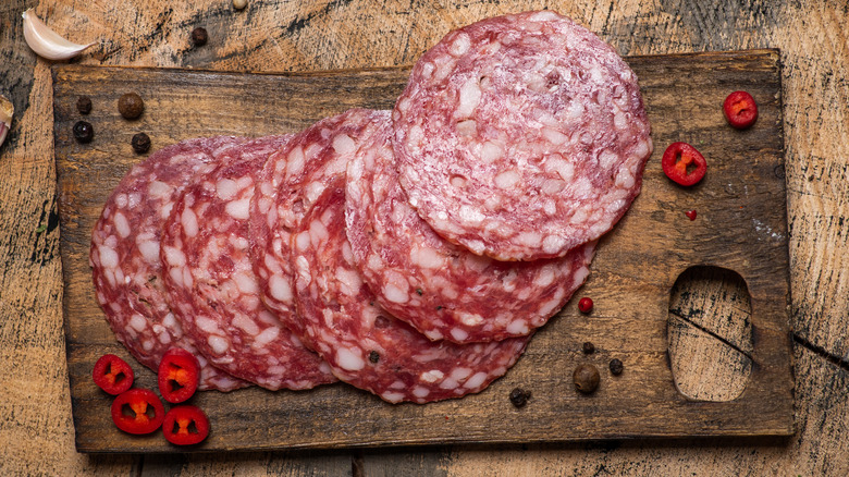 Sliced salami on a wooden board with red pepper slices and garlic