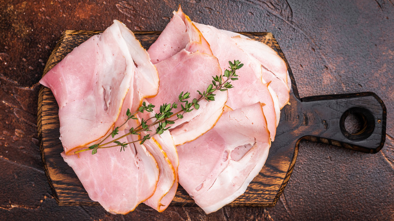 Prosciutto cotto sliced on a wooden board topped with thyme