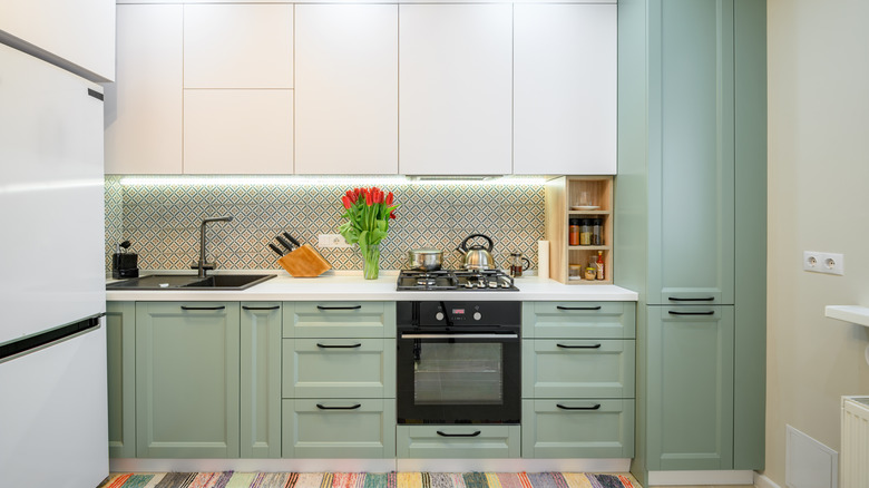 A small kitchen has sage green cabinets on bottom and white cabinets on top.