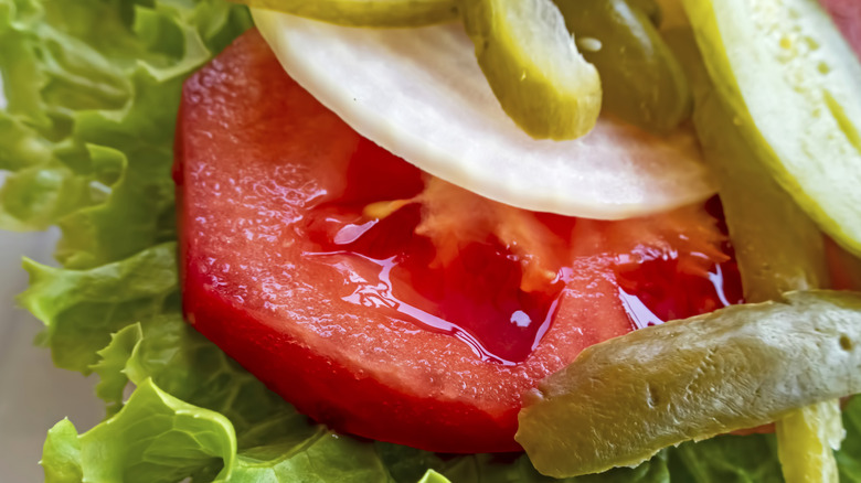 Sliced pickles, onion, and tomato atop a leaf of lettuce