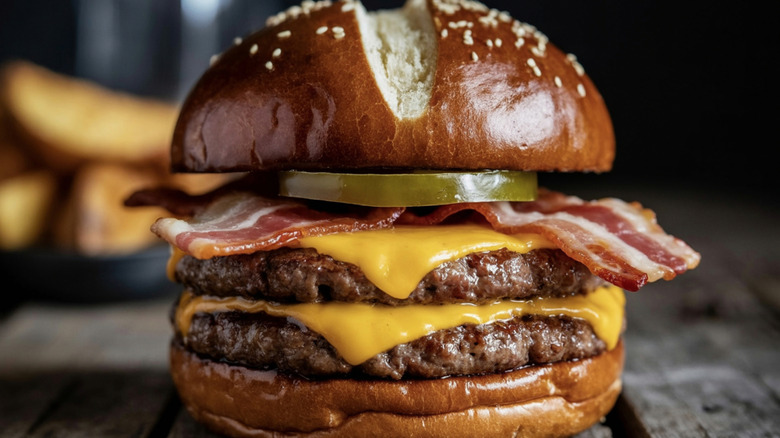 A double cheeseburger with bacon and pickle on a sesame seed pretzel bun