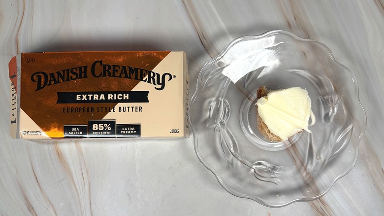 Package of Danish Creamery salted butter next to glass plate with piece of baguette and butter