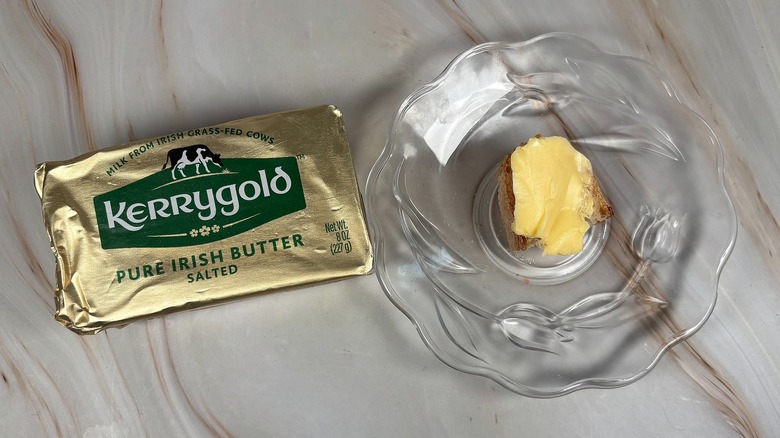 Package of Kerrygold salted butter next to glass plate with piece of baguette and butter