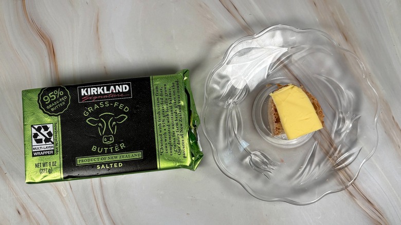 Package of Kirkland salted butter next to glass plate with piece of baguette and butter