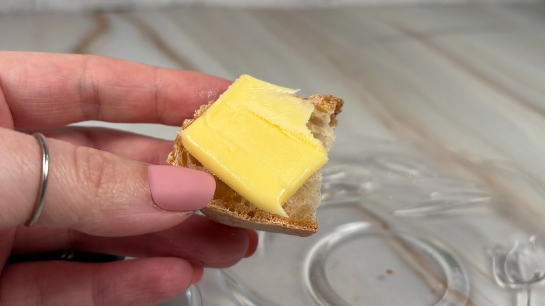 Close-up of hand holding piece of baguette with pat of butter on top