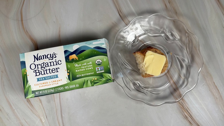 Package of Nancy's salted butter next to glass plate with piece of baguette and butter